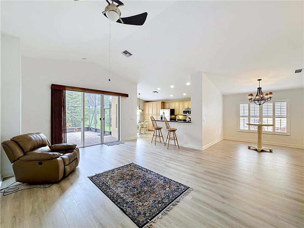 Spacious living area featuring vaulted ceilings, light wood-finish flooring, and direct patio access through sliding glass doors