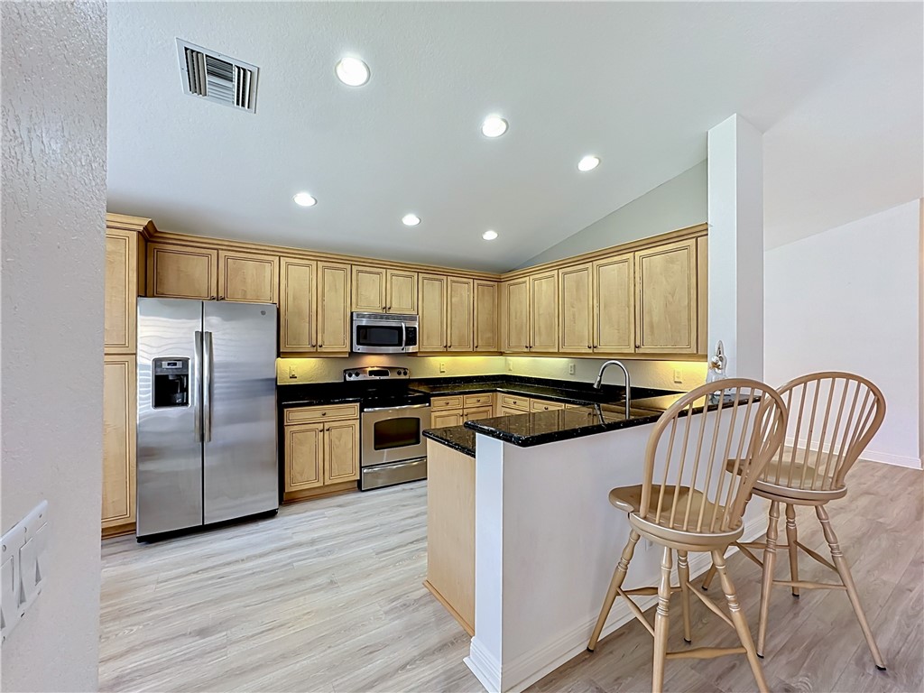 Kitchen featuring light wood cabinetry, dark granite countertops, stainless steel appliances, recessed ceiling lighting, and wood-finish flooring