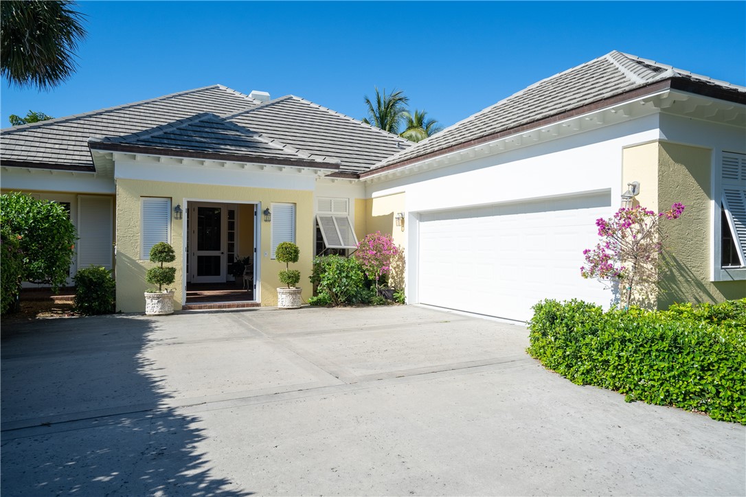 Yellow stucco exterior with a tiled hip roof, featuring a concrete driveway, an integrated garage with a white door, and a covered entry with a glass-paned door
