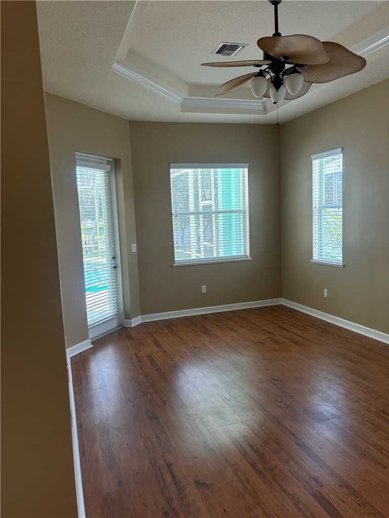 Spacious room featuring wood-finish flooring, a tray ceiling with crown molding, and a tropical-style ceiling fan