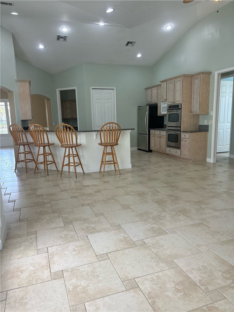 Spacious kitchen and dining area featuring vaulted ceilings, recessed lighting, tile flooring, a breakfast bar, and wood-finish cabinetry with dark countertops