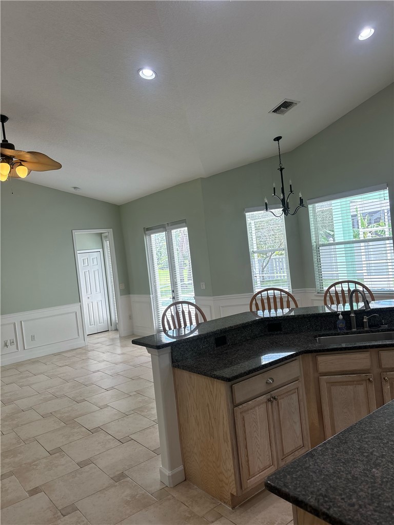 Kitchen island with dark granite countertops, light wood cabinetry, and integrated breakfast bar seating