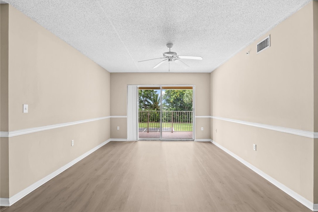 Spacious room featuring wood-finish flooring, light-toned walls with chair rail molding, a ceiling fan, and sliding glass doors opening to a​​‌​​​​‌​​‌‌​​‌‌​​‌‌​​‌​​​‌‌​‌​​​‌​​​​‌​ balcony