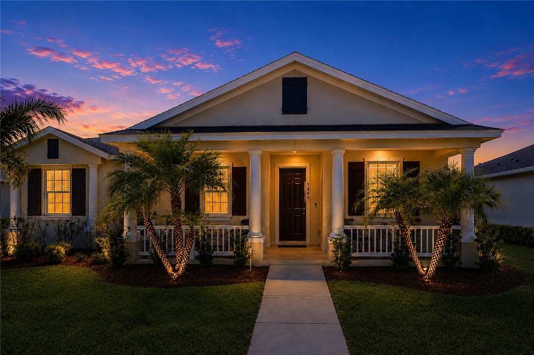 Inviting covered front porch with white columns, dark shutters, a dark paneled door, and landscape lighting