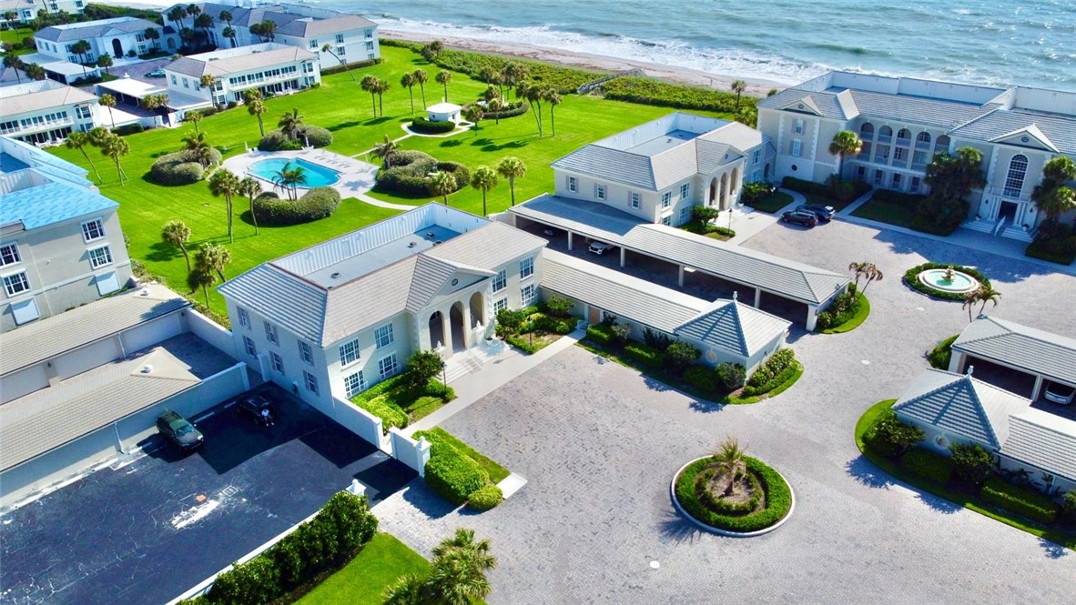 Oceanfront property featuring extensive green lawns, a swimming pool, covered parking, a paver driveway, and mature palm trees