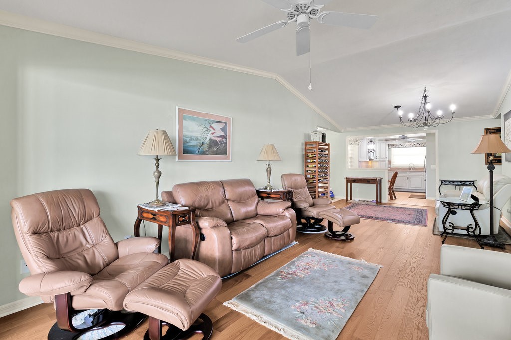 Spacious living area featuring wood-finish flooring, vaulted ceilings, a ceiling fan, and crown molding
