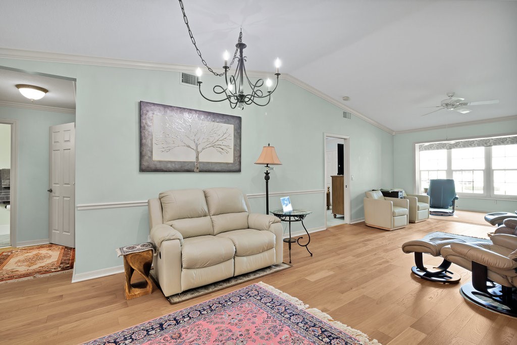 Spacious living area featuring light wood-finish flooring, vaulted ceilings, and crown molding
