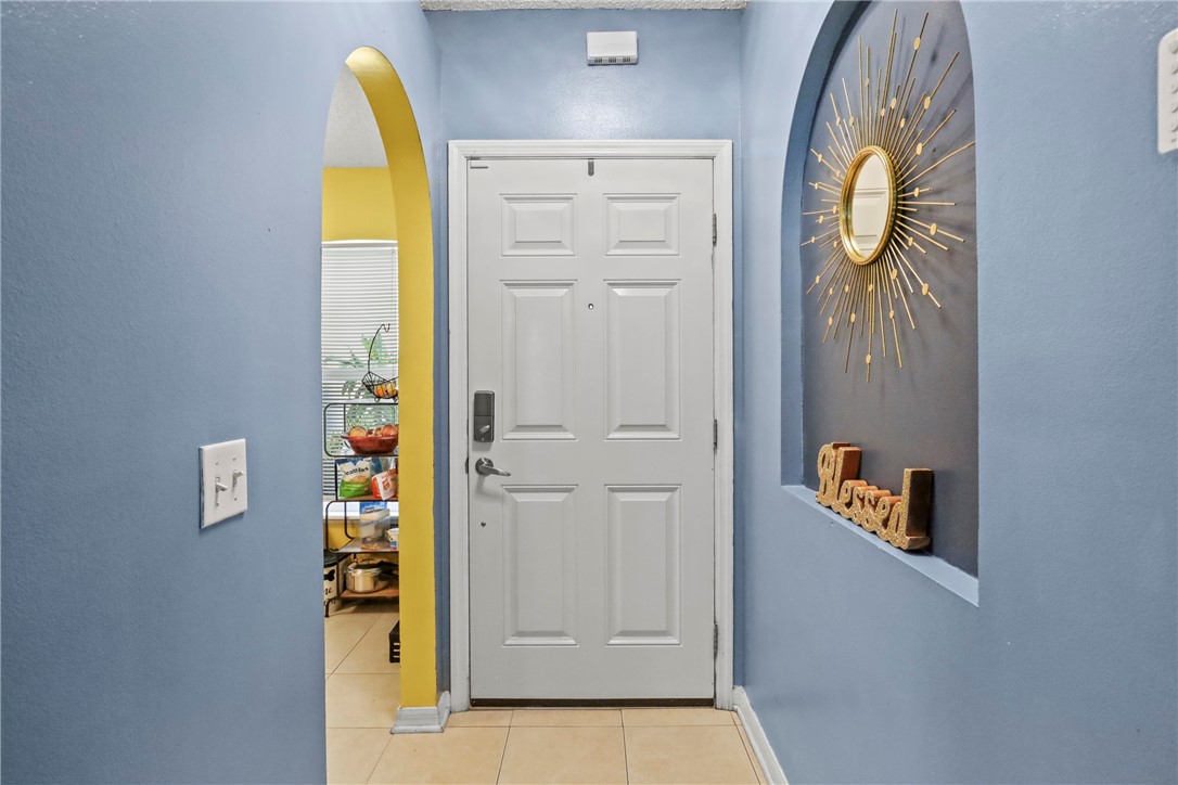 Entryway featuring a paneled door with a smart lock, an arched doorway, and tile flooring