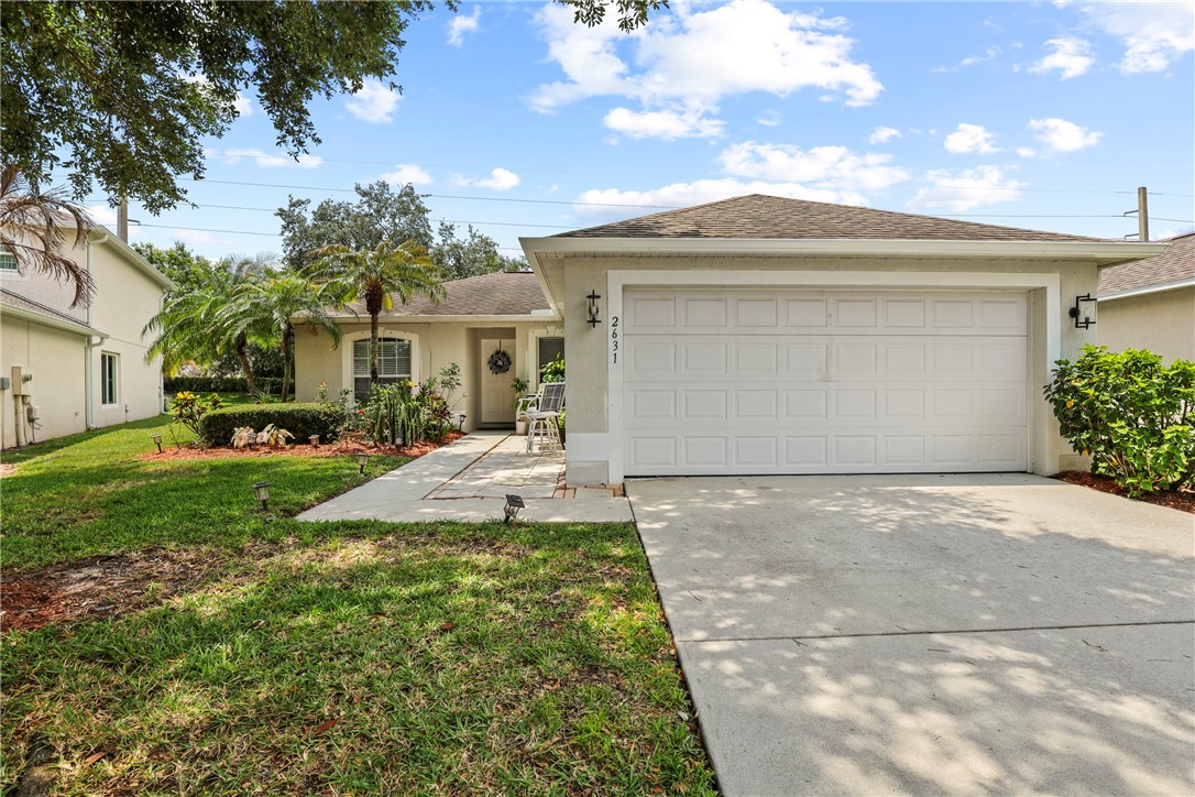 Single-story residence featuring a two-car garage, concrete driveway, and a front yard with established landscaping including palm trees