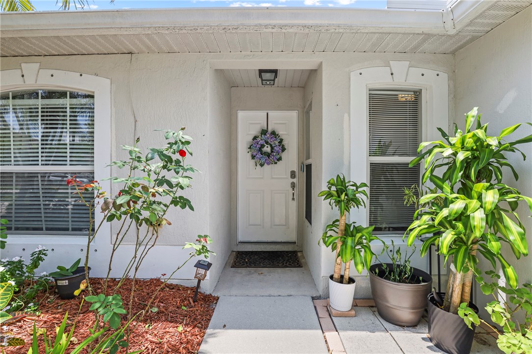 Inviting front entry featuring a white door, twin windows with blinds, and decorative landscaping