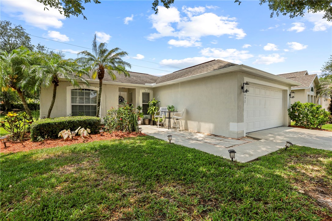 Single-story residence featuring a two-car garage with a paneled door, a paved driveway, and a front yard with mature palm trees and manicured shrubs