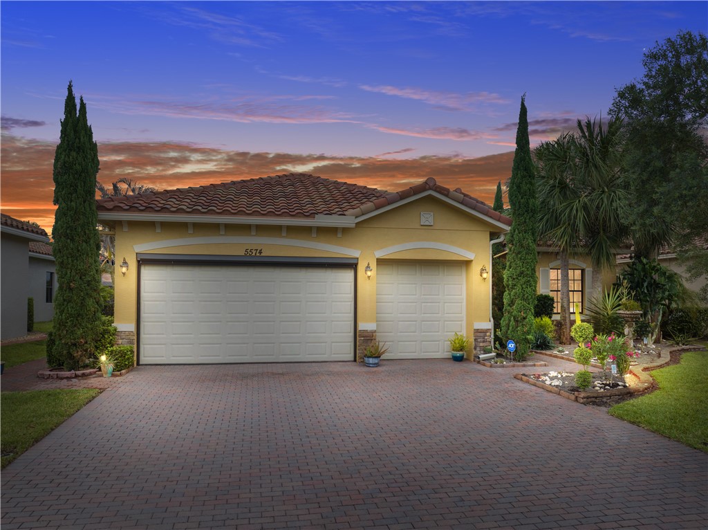 Mediterranean-style residence featuring a terracotta tile roof, a paver driveway, an attached two-car garage, and established landscaping