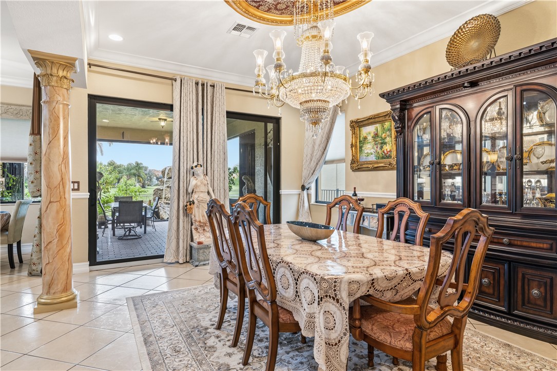 Interior dining area featuring a prominent crystal chandelier with a gold-tone ceiling medallion, light-toned tiled flooring, and a sliding glass door opening to a tiled patio