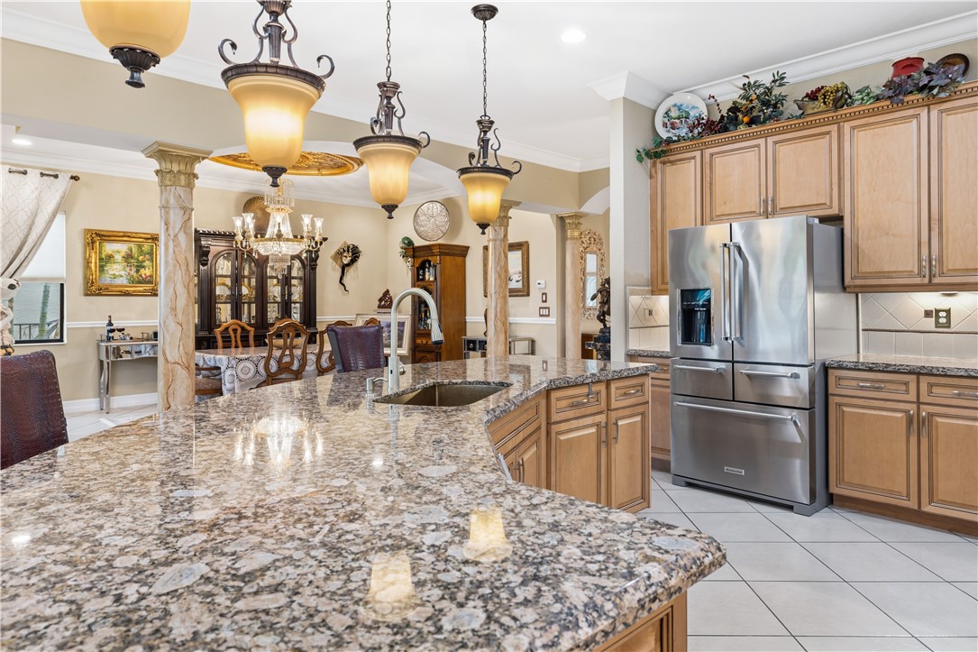 Granite countertop island with an undermount sink, stainless steel appliances, wood cabinetry, tile flooring, and decorative pendant lighting