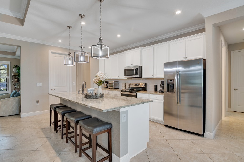 Kitchen featuring a large central island with seating, pendant lighting, stainless steel appliances, white cabinetry, and tile flooring
