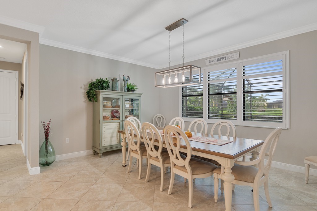 Dining area featuring neutral wall tones, large window with white plantation shutters, and a multi-bulb linear chandelier