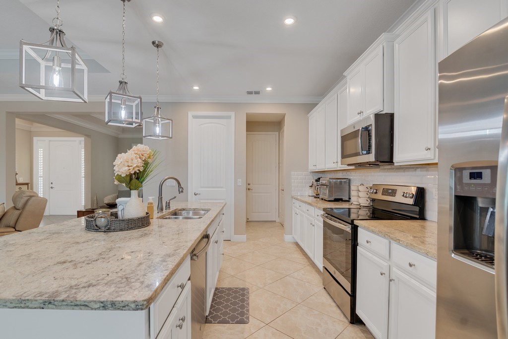 Kitchen featuring an island with ample countertop space, a double basin sink with a gooseneck faucet, and three pendant light fixtures