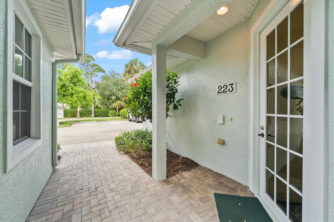 Entryway featuring a white grid-paneled door, textured exterior siding, recessed lighting, a paver walkway, and surrounding mature landscaping