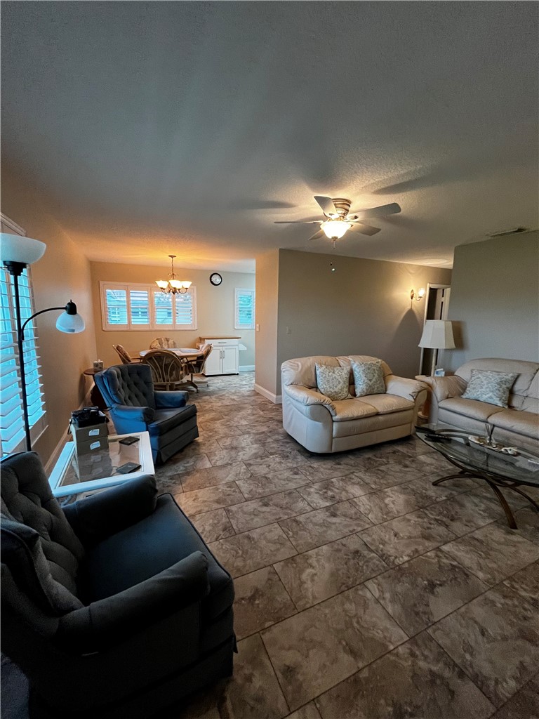 Spacious living area featuring large format floor tiling, a ceiling fan with integrated lighting, and multiple wall-mounted light fixtures