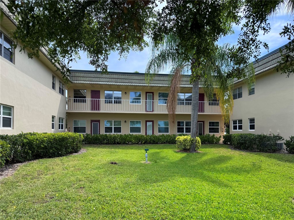 Two-story building featuring stucco exterior, multiple windows, and a green tile roof