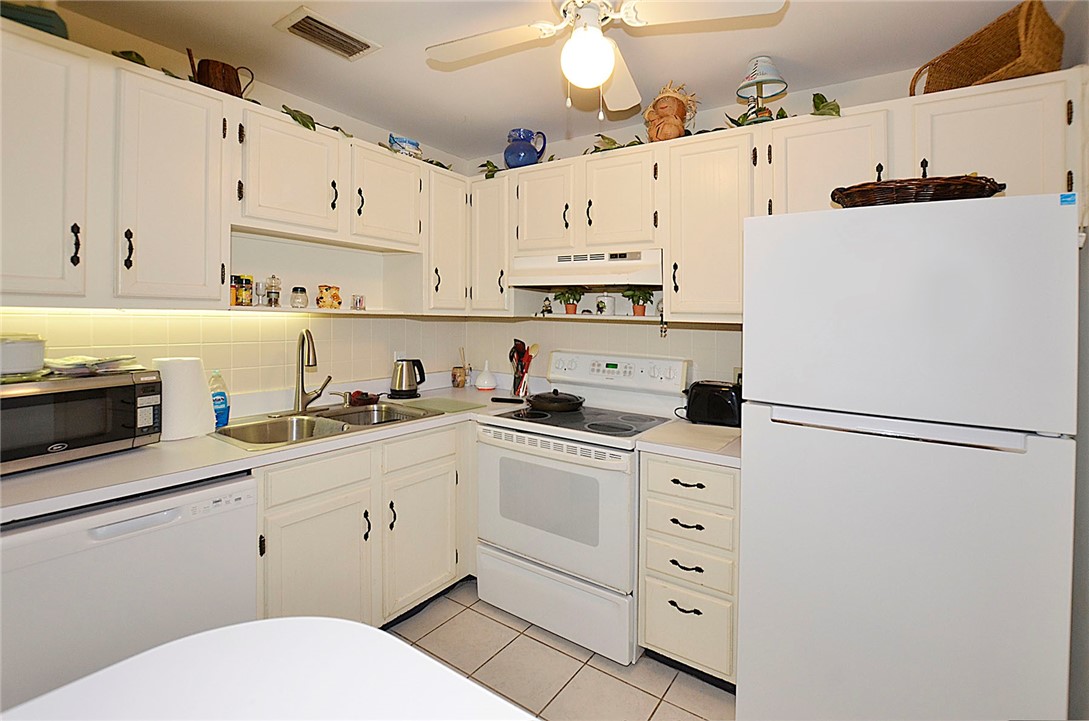 Kitchen featuring white cabinetry with dark hardware, a double basin stainless steel sink, tiled backsplash, white appliances, and a ceiling fan