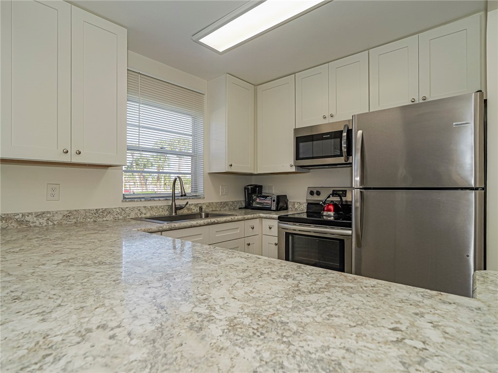 Kitchen with stainless steel appliances, white cabinetry, and light stone countertops