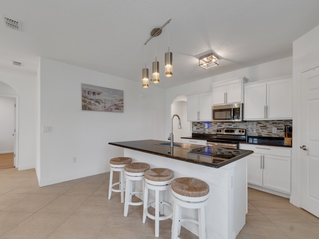 Spacious kitchen featuring a central island with a dark countertop and pendant lighting, white cabinetry, stainless steel appliances, and a mosaic tile backsplash