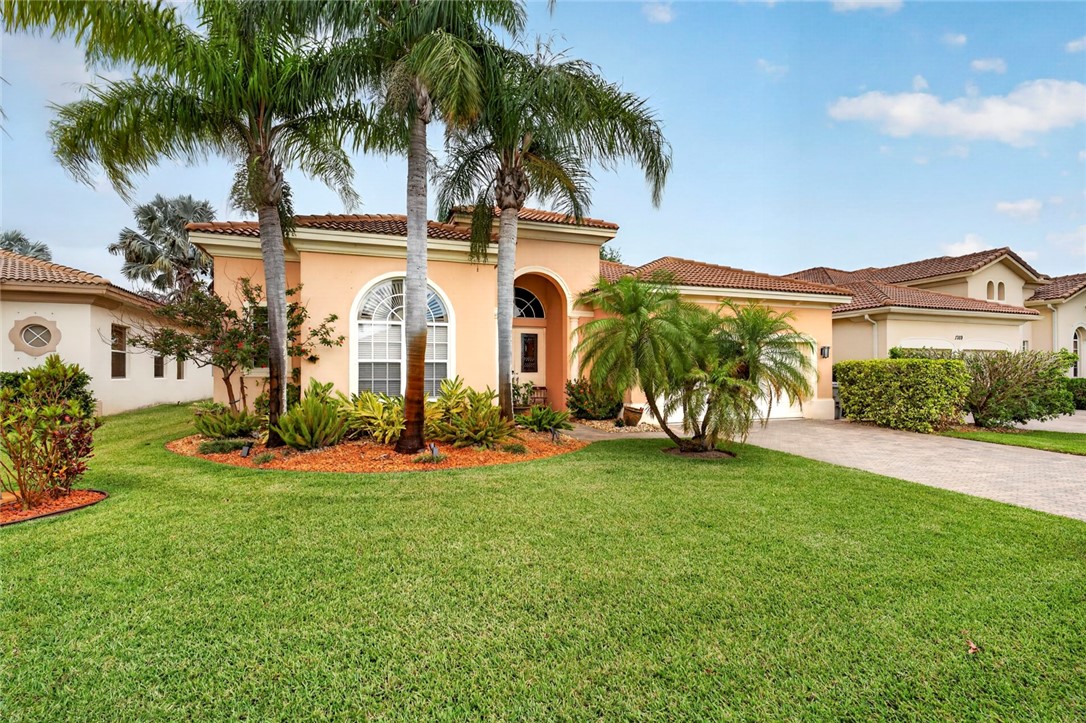 Mediterranean-style stucco exterior with a terra cotta tile roof, arched windows, and a paver driveway
