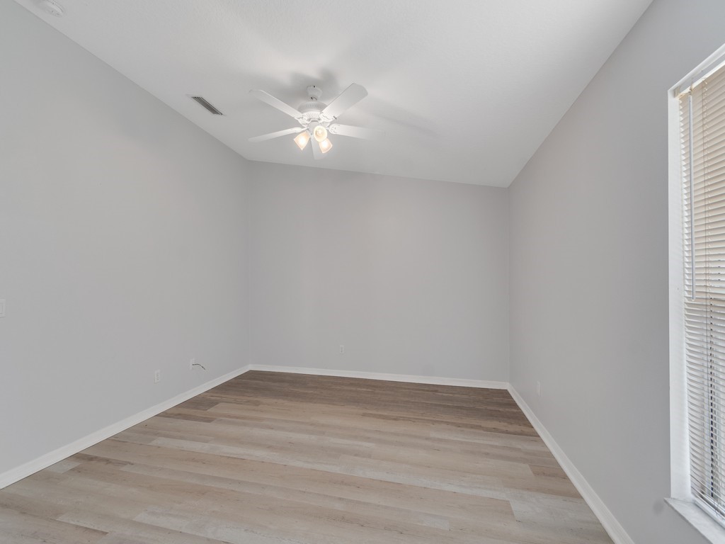 Bright interior space featuring light wood-finish flooring, neutral gray walls, a white ceiling fan with integrated lighting, and a window with horizontal blinds