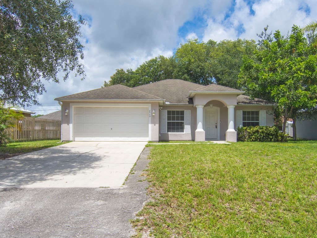 Single-story residence featuring a two-car garage, covered entry with columns, white window shutters, and a green lawn
