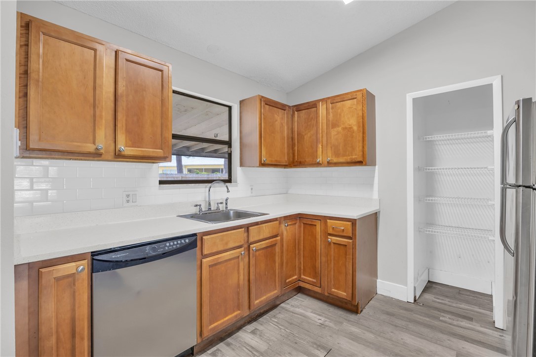 Kitchen featuring wood cabinetry, white subway tile backsplash, light-toned countertops, a stainless steel sink with a gooseneck faucet, and wood-finish flooring