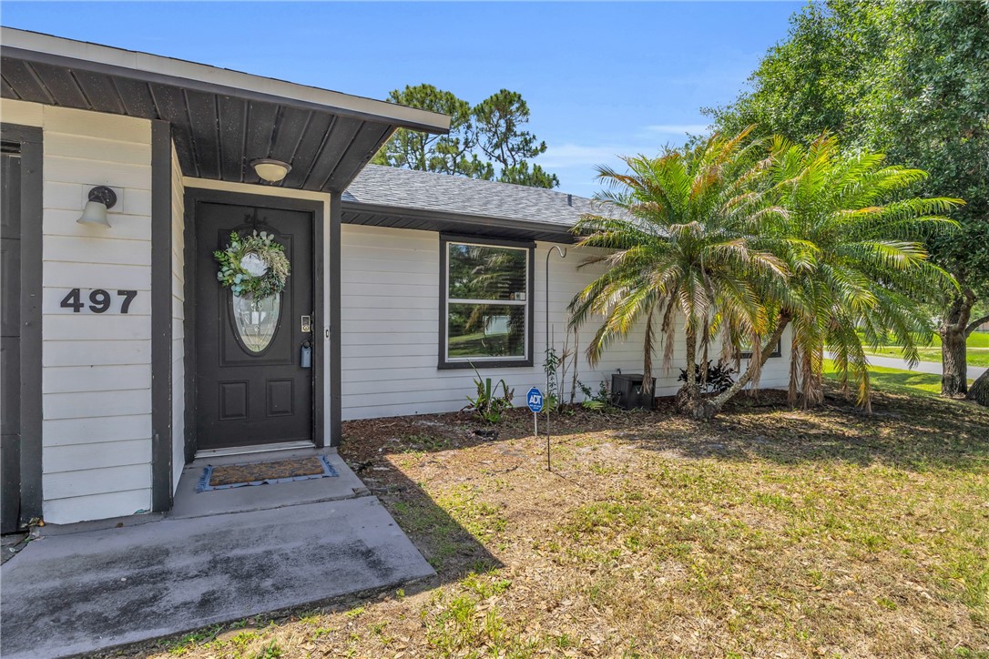 White horizontal siding exterior featuring a dark entry door with an oval glass insert, a complementary dark trim, and mature palm trees