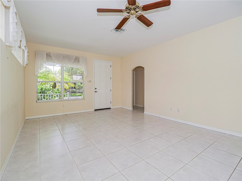 Tile flooring, white paneled entry door, arched doorway, ceiling fan, and large window