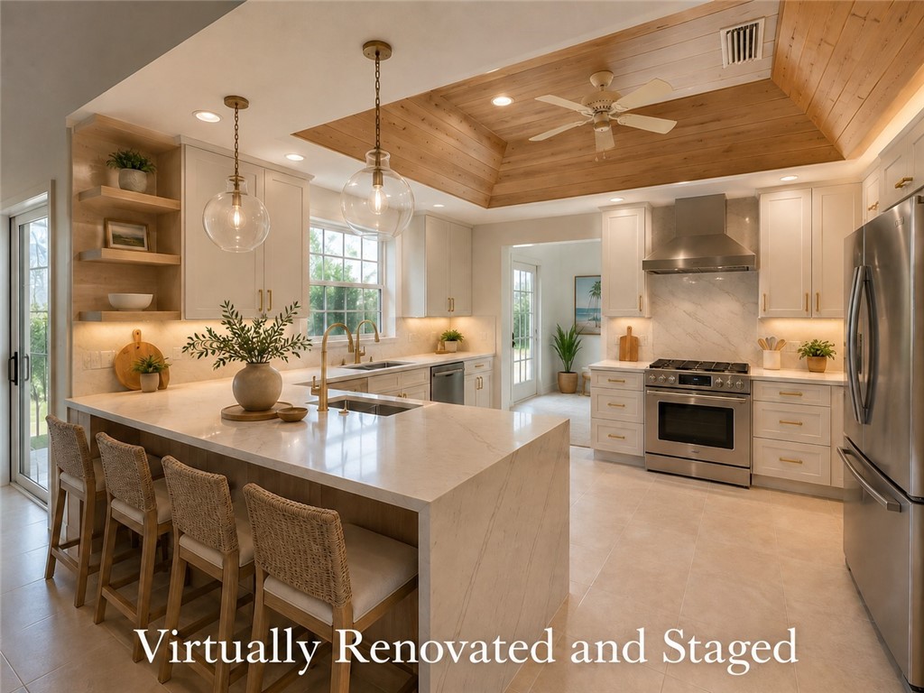 Spacious kitchen featuring an extended island with waterfall countertop, wood-paneled tray ceiling, stainless steel appliances, white cabinetry with gold-tone hardware, and light-toned tile flooring