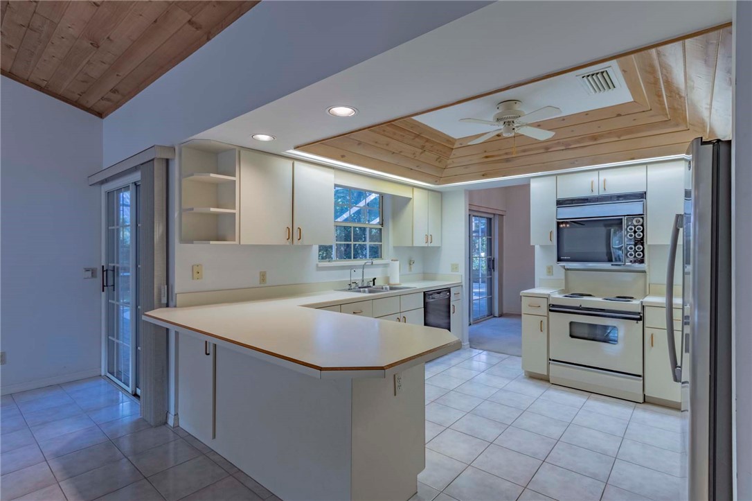 Kitchen featuring a U-shaped countertop, white cabinetry, and a wood-paneled ceiling with recessed lighting. Dual ovens- 1 in range bottom and 1 over the burners