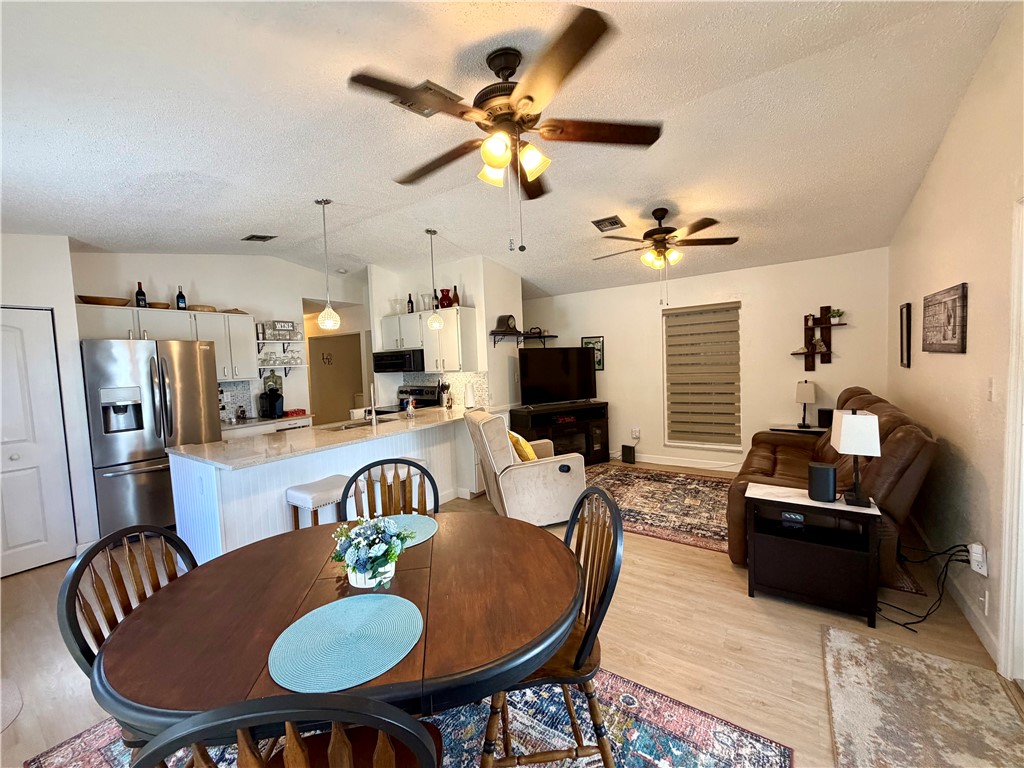 This open-concept living space features vaulted ceilings with ceiling fans, light-toned flooring, and a kitchen with white cabinetry and stainless steel appliances