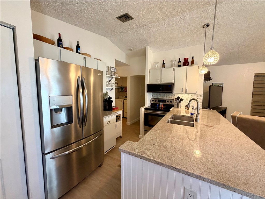 The kitchen features a stainless steel refrigerator, white cabinetry, a kitchen island with a sink and a light-colored countertop, and a stovetop with an overhead microwave