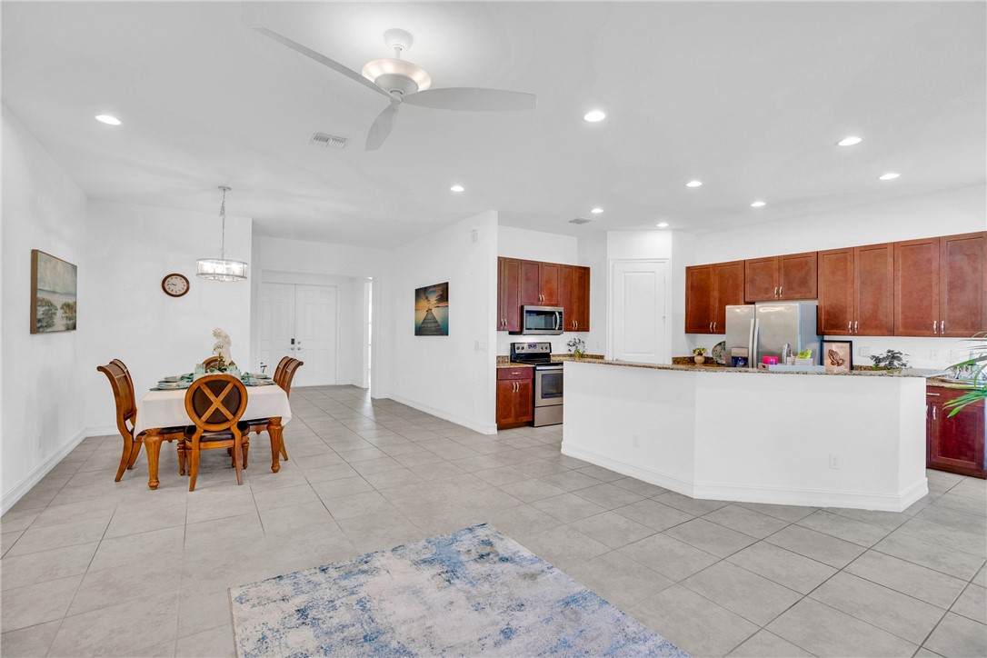 Kitchen with ceiling fan, stainless steel appliances, a center island with sink, light stone counters, and decorative light fixtures
