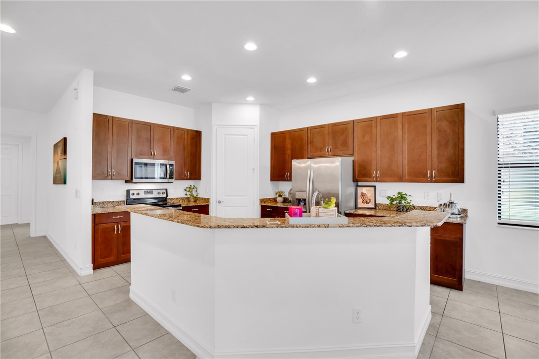 Kitchen featuring light stone countertops, light tile patterned floors, stainless steel appliances, a large island with sink, and recessed lighting