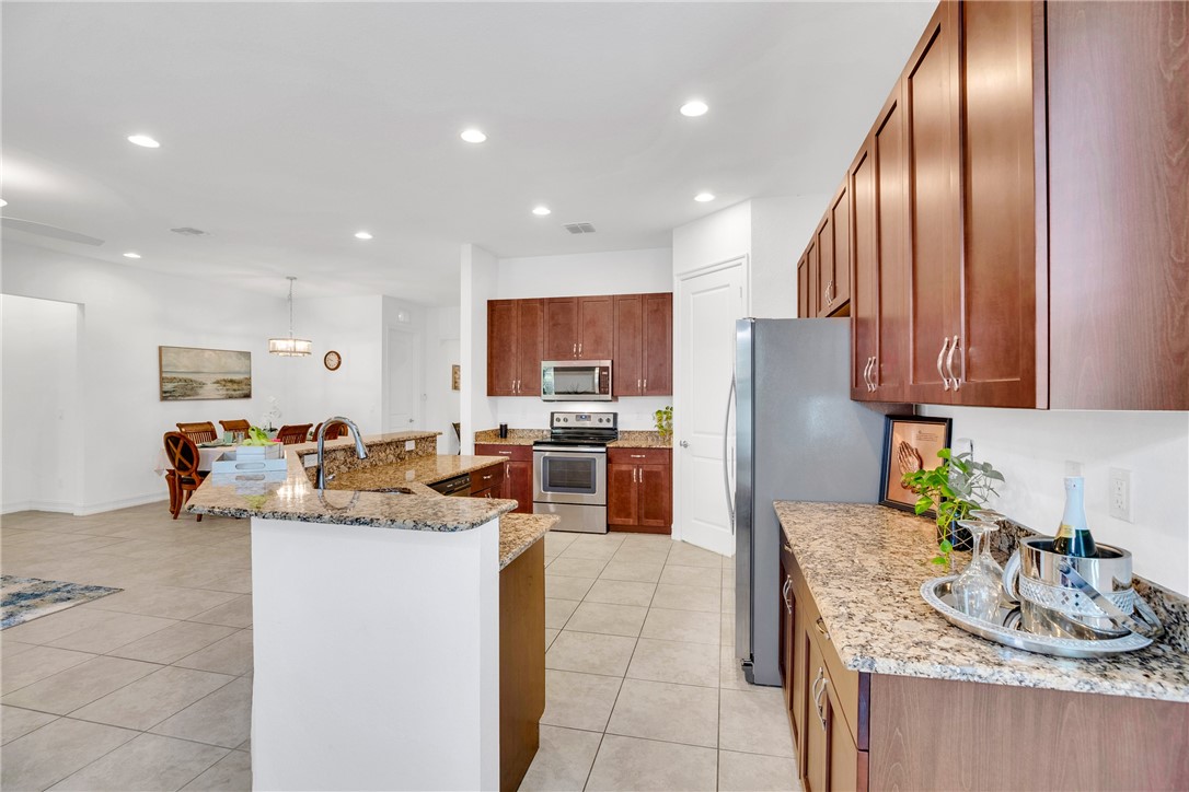 Kitchen featuring stainless steel appliances, a large island with sink, light stone countertops, light tile patterned floors, and hanging light fixtures