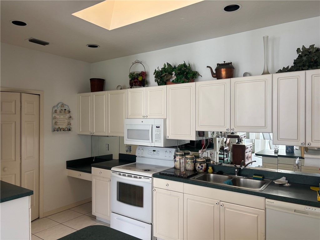 Kitchen with white appliances, dark countertops, light tile patterned floors, and white cabinets