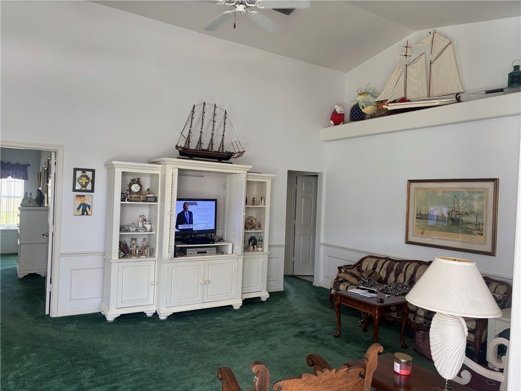 Living area featuring a wainscoted wall, dark colored carpet, ceiling fan, a decorative wall, and vaulted ceiling
