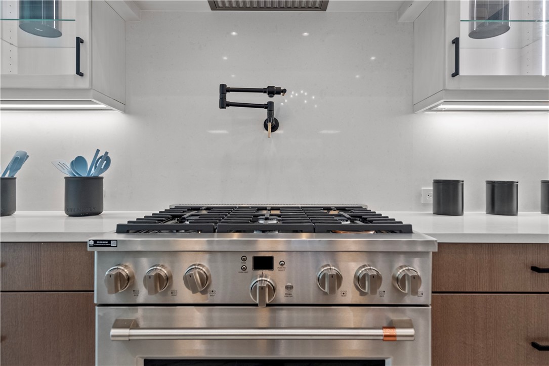 Kitchen view of high end range, pot filler, modern cabinets, and light stone countertops