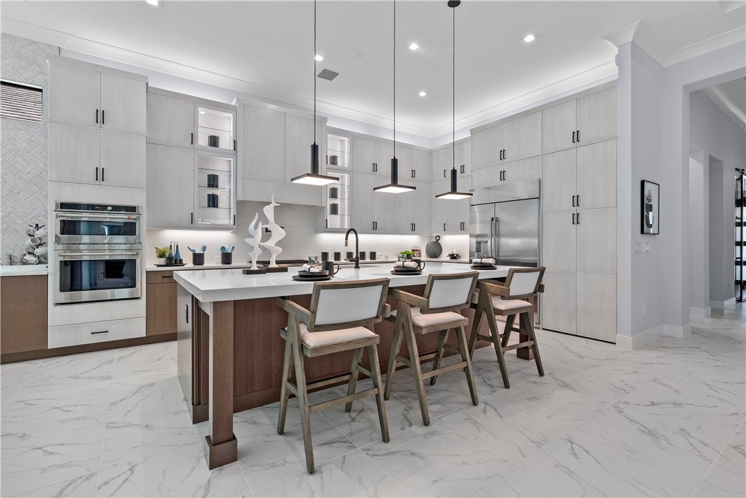 Kitchen featuring a breakfast bar, light marble finish floors, ornamental molding, stainless steel double oven, and an island with sink