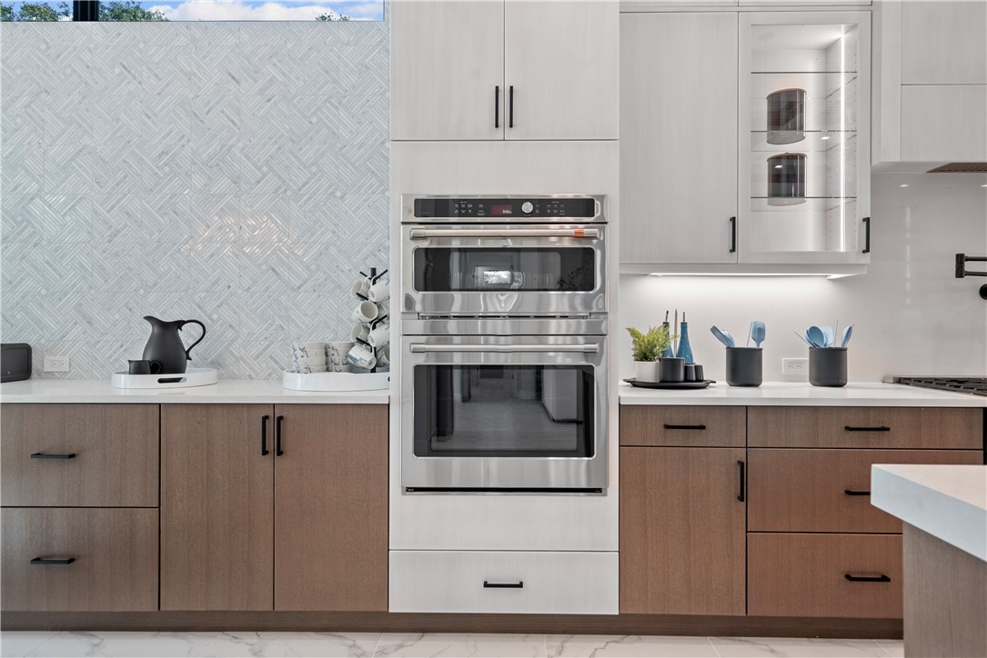Kitchen with double oven, modern cabinets, light stone countertops, glass fronted cabinets, and two tone cabinets