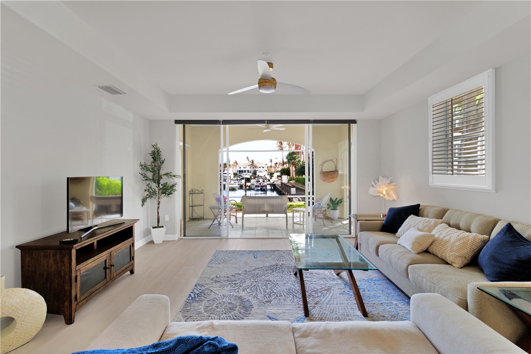 Living room featuring a ceiling fan, a raised ceiling, healthy amount of natural light, and wood finished floors