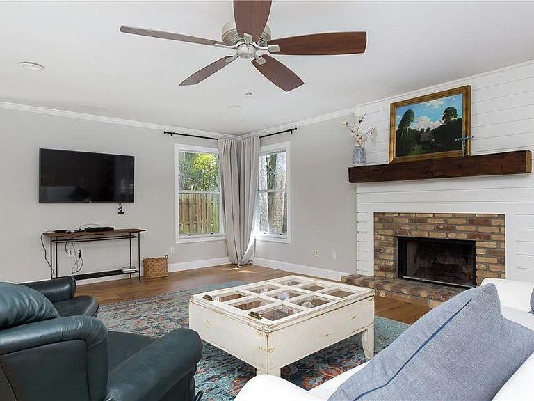 Living area featuring dark wood-style floors, a ceiling fan, crown molding, and a fireplace