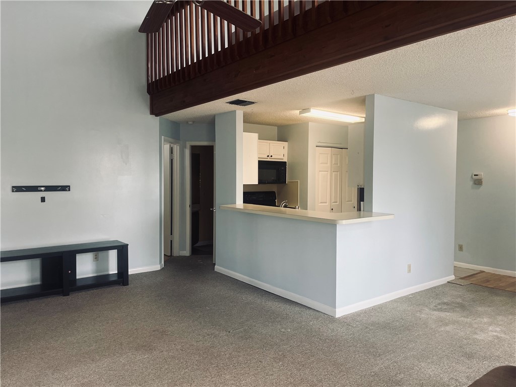 Open-concept layout with a breakfast bar, kitchen cabinetry with built-in microwave, and an upper-level wood railing