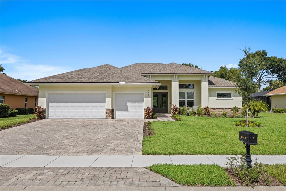 Stucco exterior with stone accents, paver driveway, two-car garage, and established landscaping