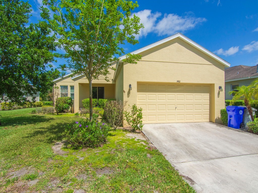 The property features a front yard with mature trees and landscaping, a concrete driveway, and an attached garage